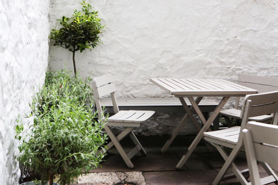 Terraza con mesa y sillas junto a una pared blanca