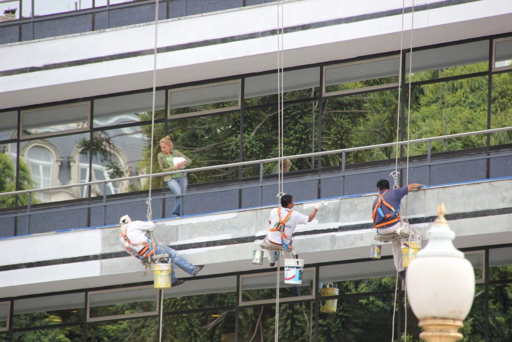 Operarios colgados de cuerdas pintando la fachada de un edificio en descuelgue